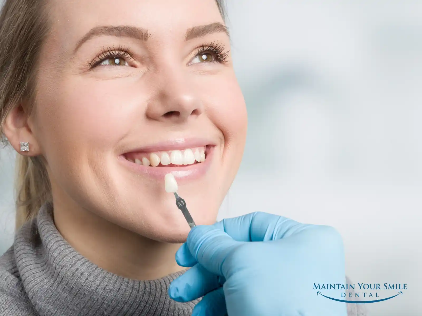 Cosmetic dentist holding a porcelain veneer shade guide next to a smiling patient's teeth at Maintain Your Smile in Rockford, IL.